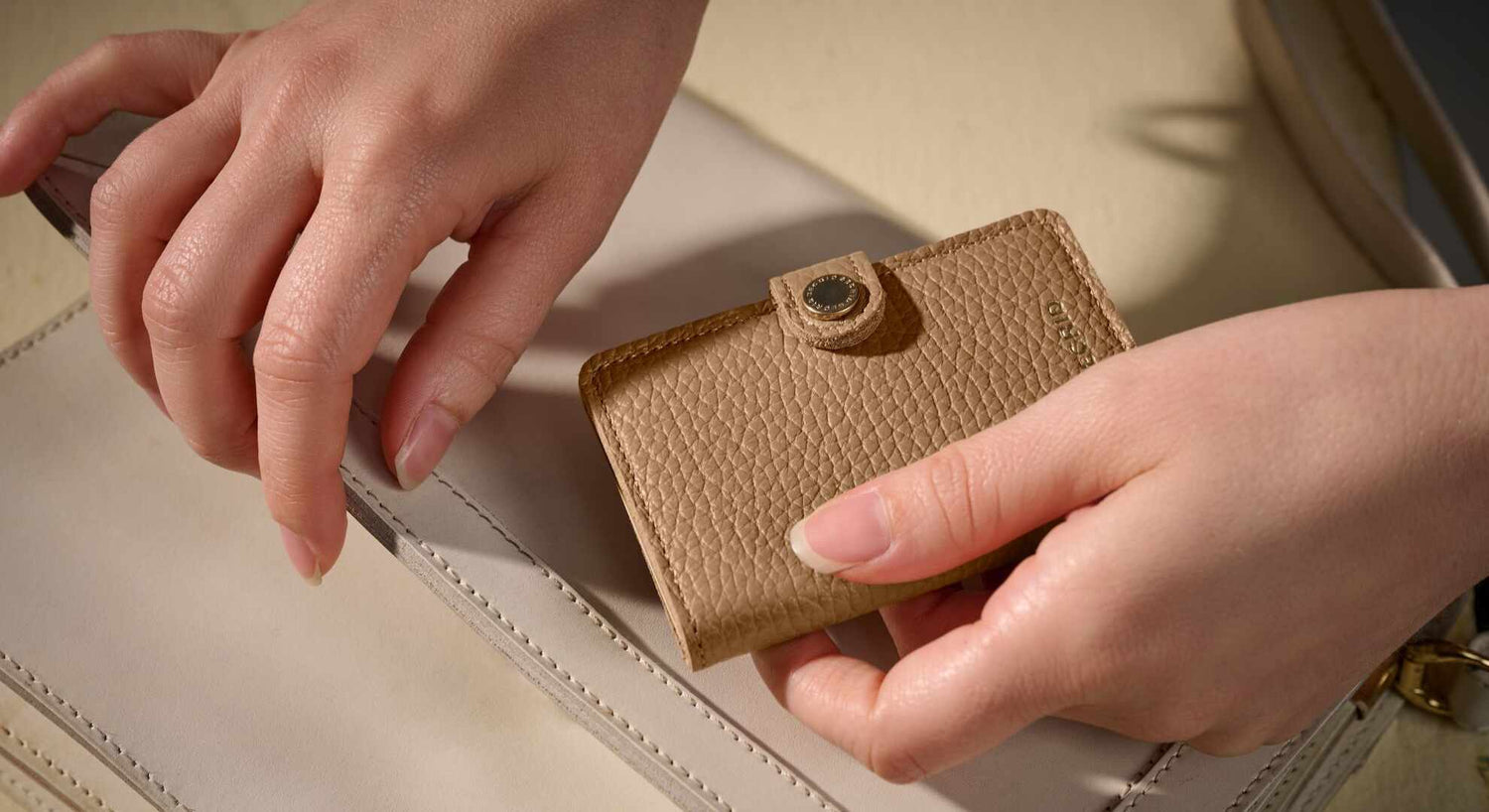 Vrouw haalt beige Secrid pasjeshouder dames uit haar lichte handtas