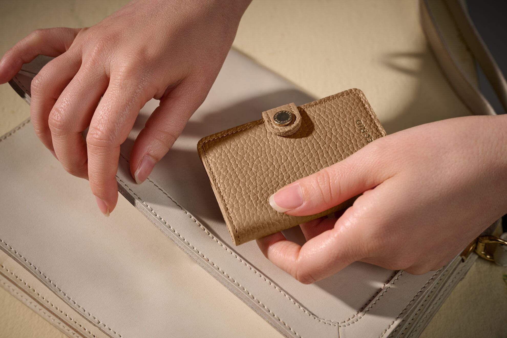 Vrouw haalt beige Secrid pasjeshouder dames uit haar lichte handtas