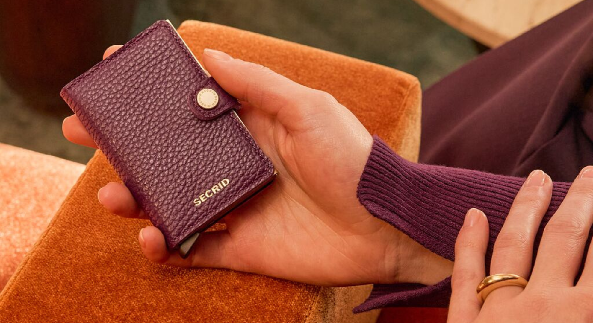 SECRID Miniwallet in paars leer, in dameshand op oranje stoel