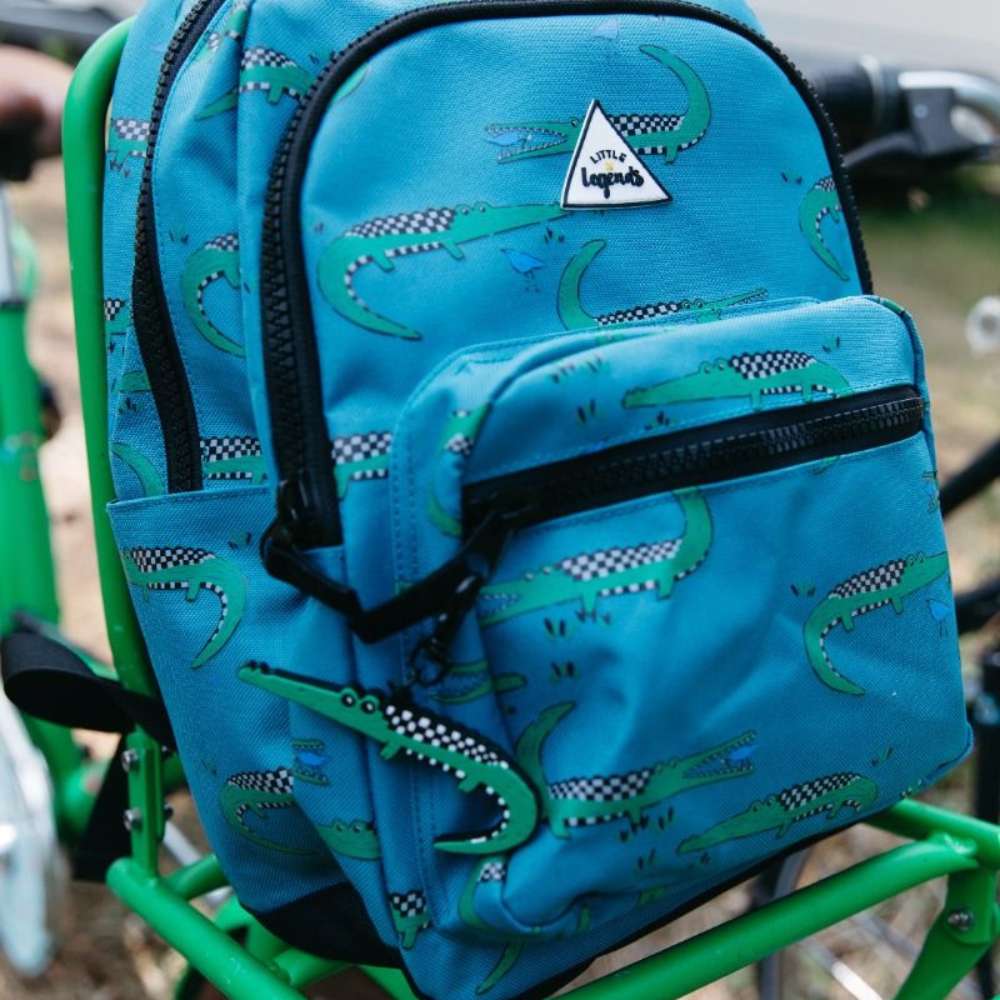 Kinderrugzak met groene krokodillen op blauwe achtergrond en checkerboard print, inclusief grappige krokodillendetails en duurzaam materiaal op fiets